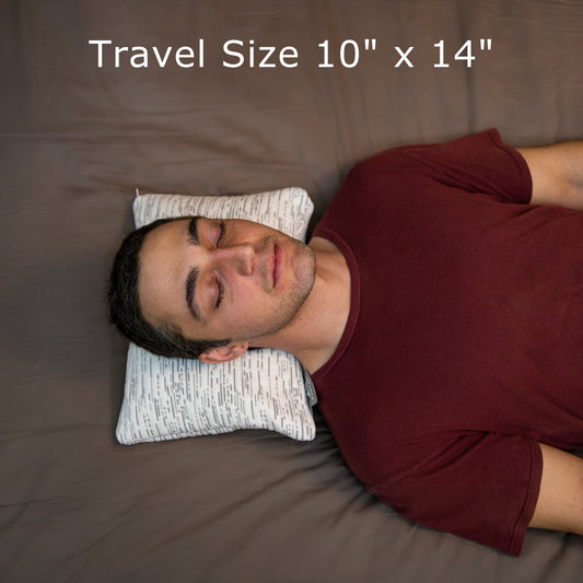 Young Man laying on his back using the travel buckwheat hull pillow illustrating it's size