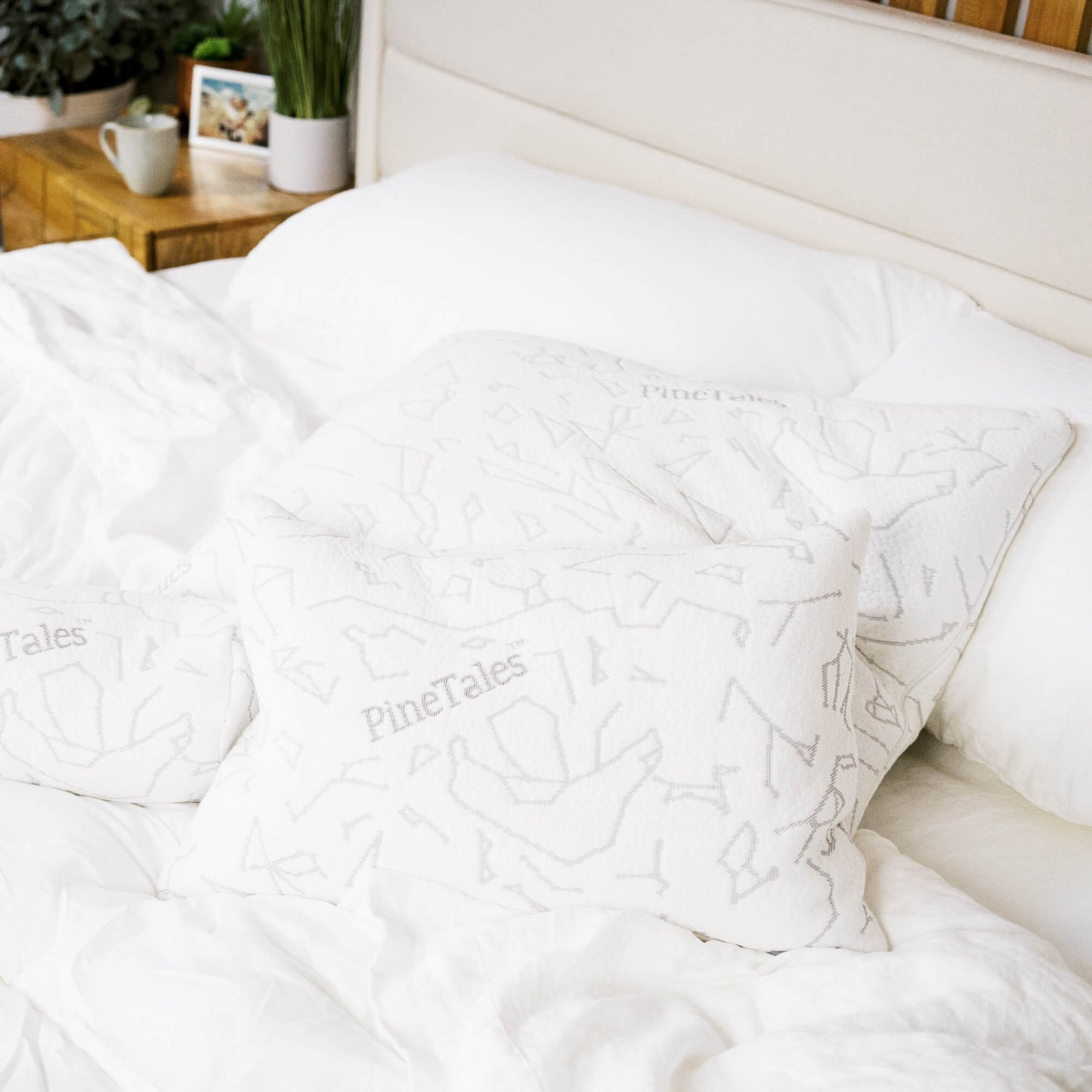 White comforter with 'PineTales' branded signature buckwheat pillows on a bed in a bedroom setting.